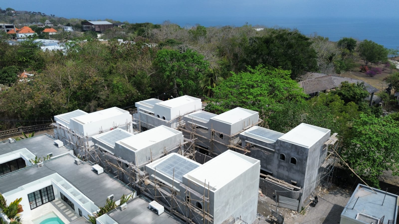 Drone view of the six villas in September 2026, with scaffolding still up and the ocean beyond